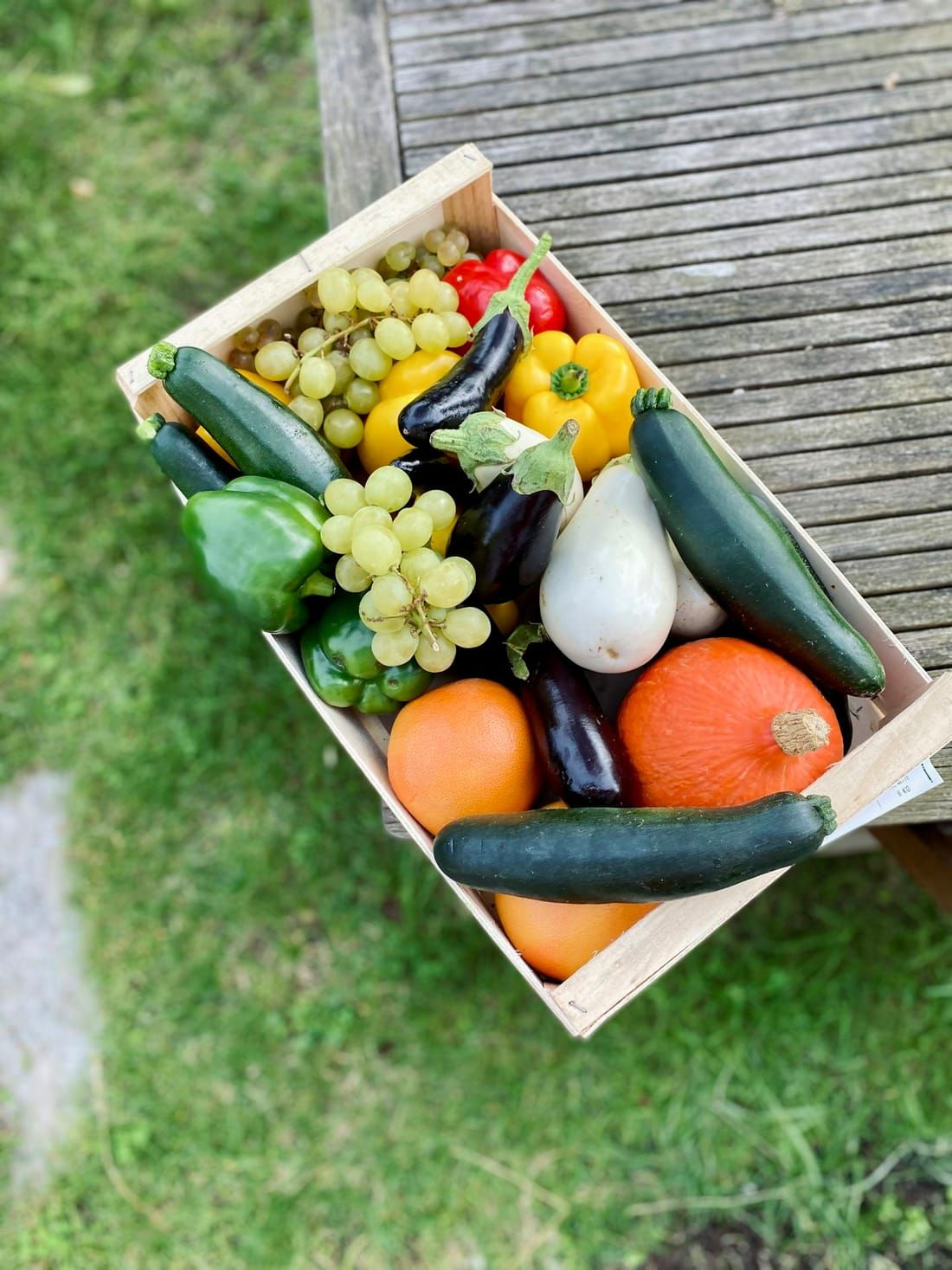 Crate of fresh vegetables and grapes on green grass